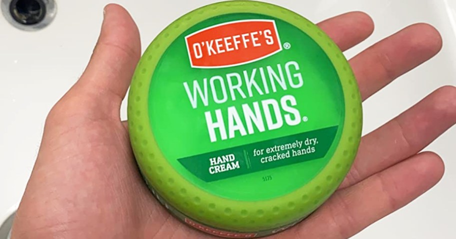hand holding a green container of O'Keeffe's Working Hands Hand Cream