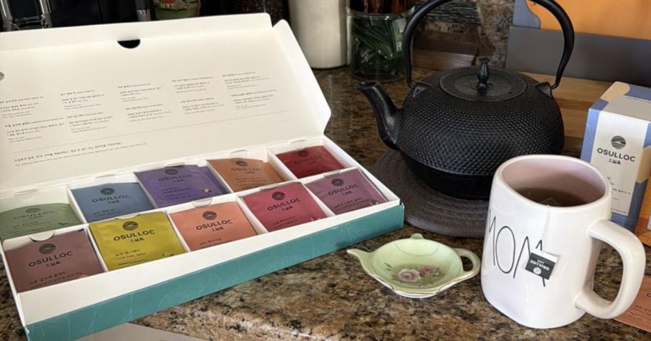 A box of Osullac Premium Tea on a counter next to a mug and a kettle