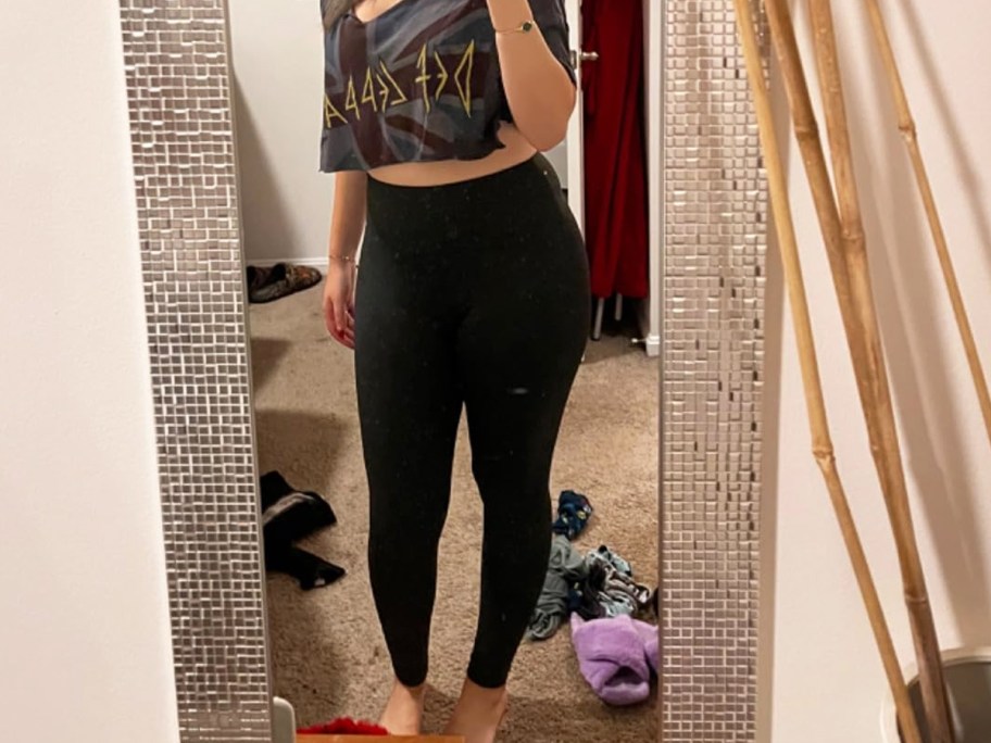 woman taking photo in mirror wearing cropped tee and black leggings