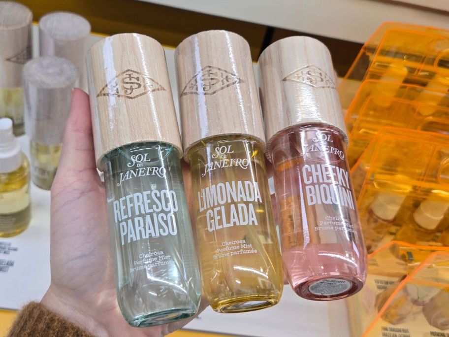Hand holding 3 bottles of Sol de Janeiro Mists in new scents