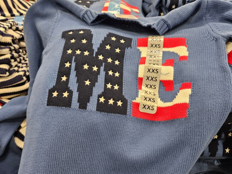 A close-up of a blue sweater featuring the letters "ME" with one letter decorated in stars and stripes.