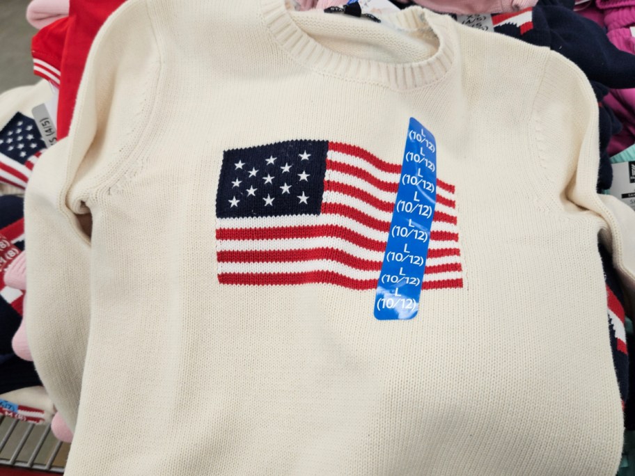 A cream-colored sweater featuring an American flag design on the front.