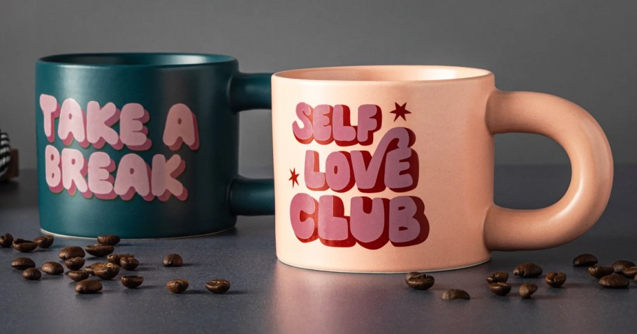 coffee mugs that say Take a Break & Self Love on a table with coffee beans