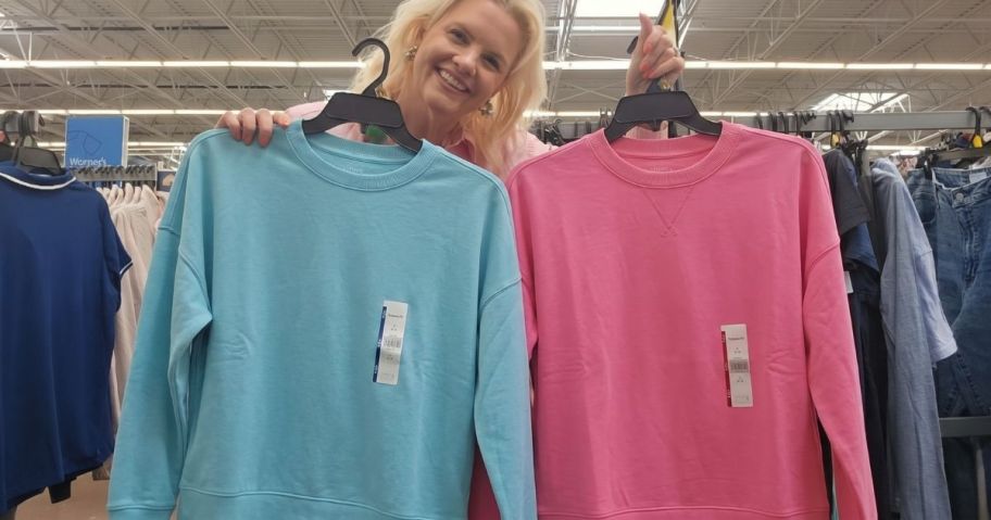 Woman holding two hangers with turquoise and pink time and true sweatshirts on them