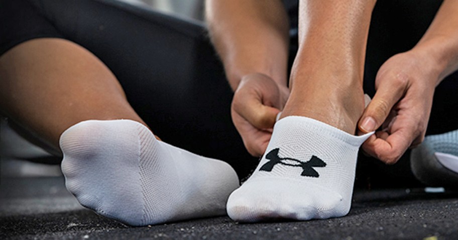 woman putting on a pair of white Under Armour socks