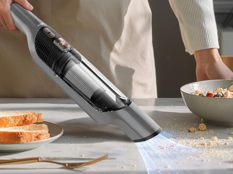 hand using a Zefiro handheld vacuum to clean up cereal crumsb next to a cereal bowl