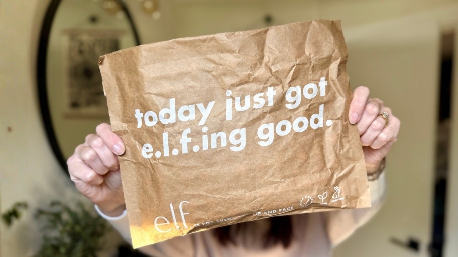a woman holding up an elf consmetics paper mailer 