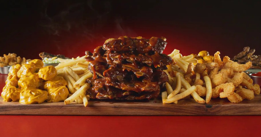 A wooden platter loaded with BBQ ribs, fries, crispy fried shrimp, and saucy wings.