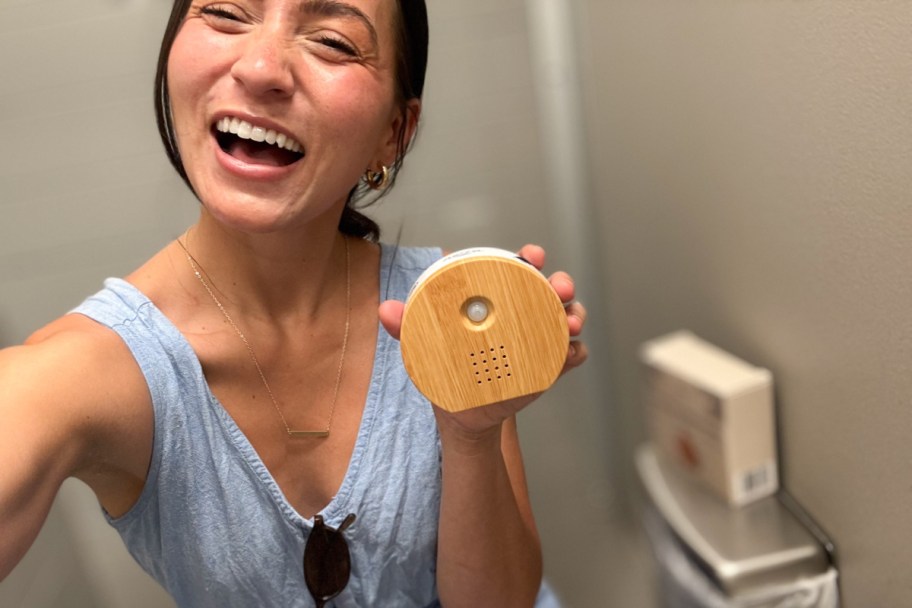 woman sitting on toilet holding bamboo round sound machine