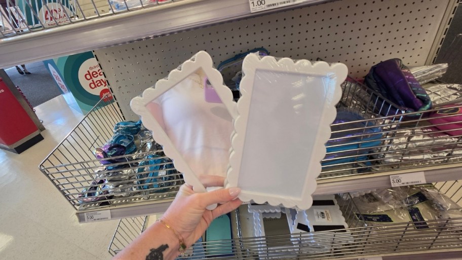 a womans hand holding a white scalloped mirrir and picture frame