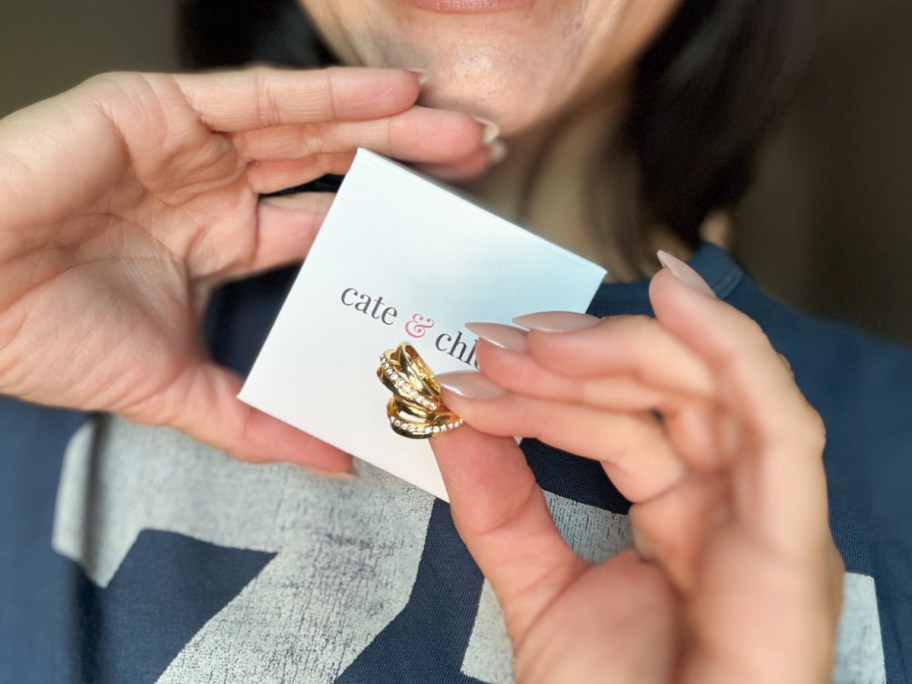 A woman holding a small white Cate & Chloe box with gold hoop earrings.