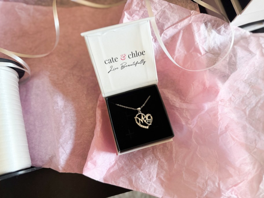 Necklace with "Mom" pendant in a Cate & Chloe box on pink tissue paper. The scene is wrapped in a gift-giving, celebratory tone.