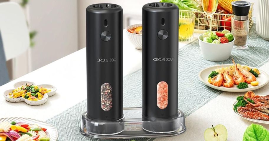 Two sleek black electric salt and pepper grinders sit on a kitchen table.