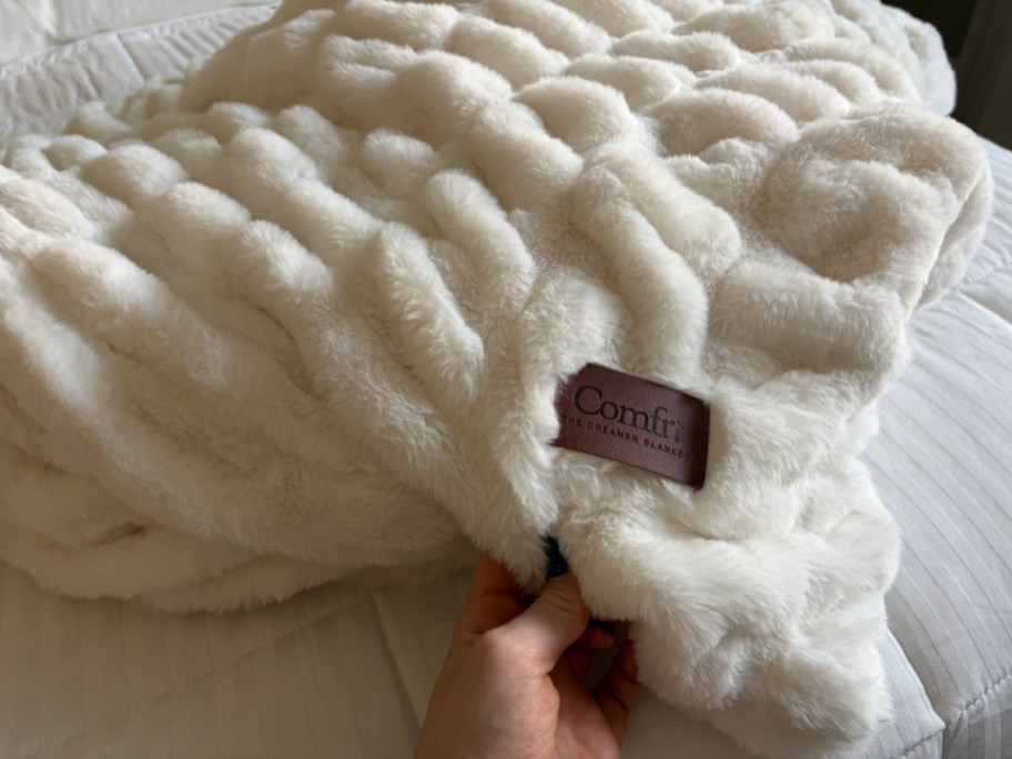 hand grabbing white textured blanket with brown tag