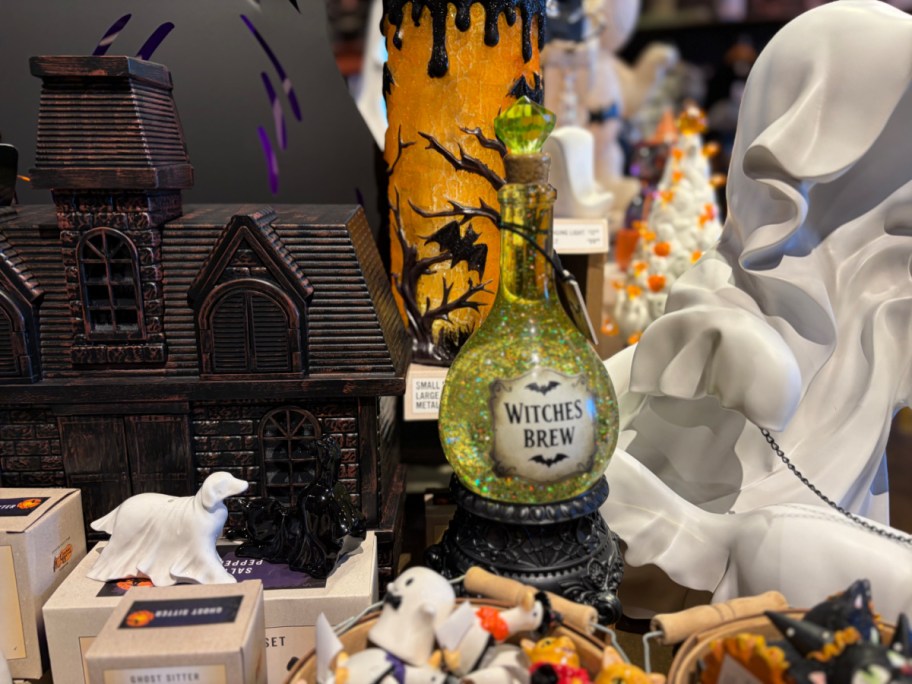 A collection of Halloween decorations, including a haunted house figurine, a spooky candle holder, a decorative bottle labeled "Witches Brew," and various other themed items.