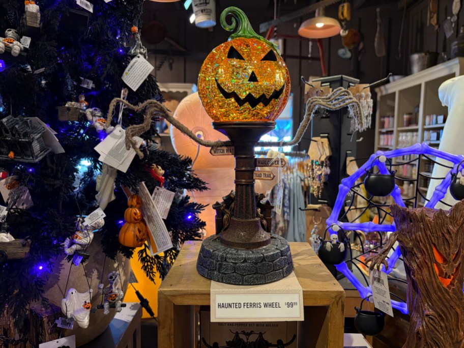 A decorative Halloween item featuring a pumpkin head on a pedestal, with ghostly arms extending from the sides, surrounded by various Halloween decorations.
