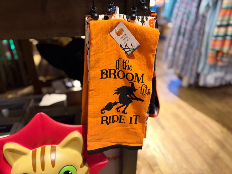 A Halloween-themed orange towel with the text "If the broom fits, ride it" displayed in a store.