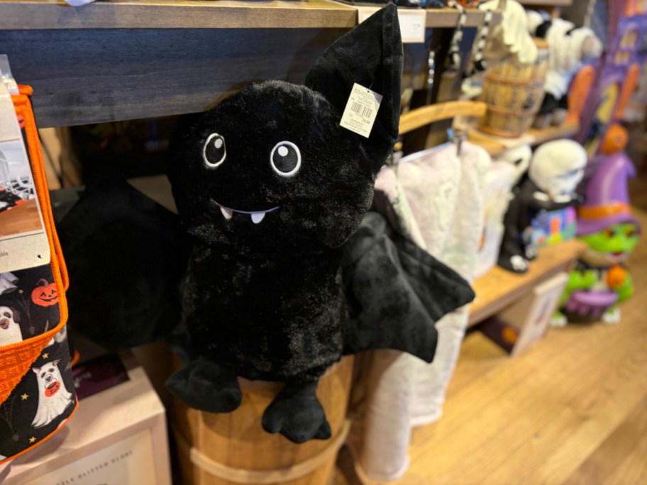 A plush bat toy with large eyes and fangs, hanging on a display in a store.