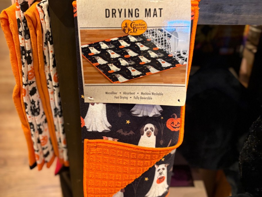 A drying mat with a Halloween theme featuring dogs and pumpkins, hanging on a display.