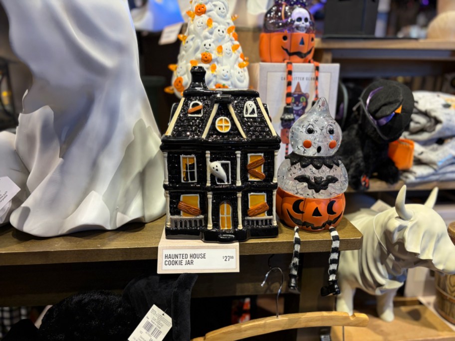 A black haunted house cookie jar with orange accents, placed on a shelf with various Halloween decorations.