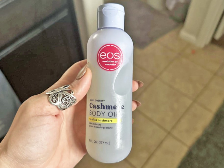 hand holding a bottle of eos Cashmere Body Oil in bathroom