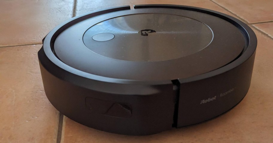 A black robotic vacuum cleaner on a tiled floor. The sleek device features a shiny top panel with a minimalist design.