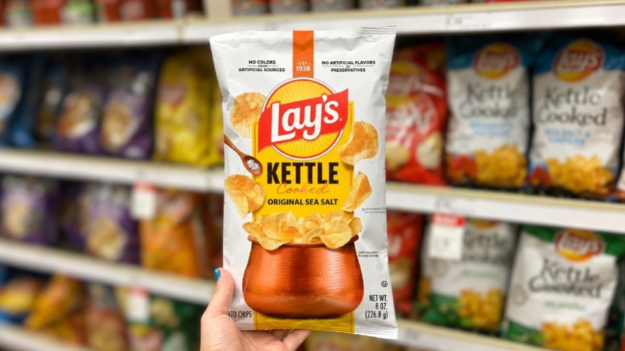 womans hand holding a bag of lays kettle chips on a store aisle