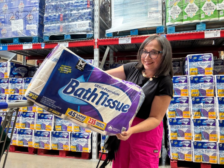 smiling woman holding an oversized package of bath tissue in a club warehouse store