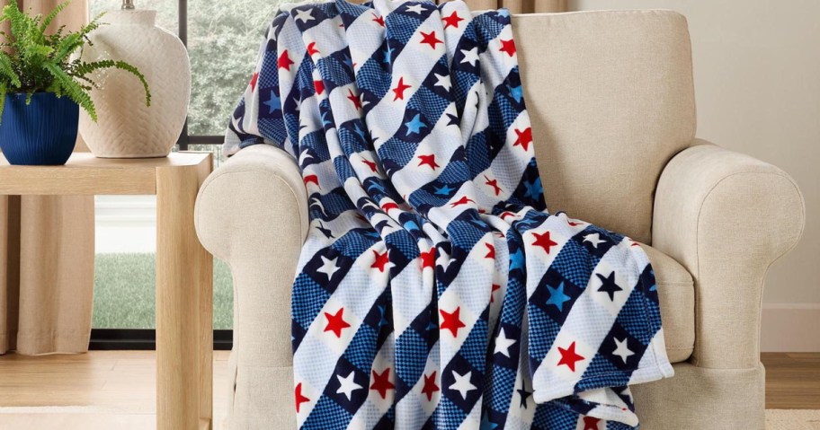 A cozy beige armchair draped with a blanket featuring a blue and white checkered pattern adorned with red and blue stars. A potted plant sits on a nearby table.