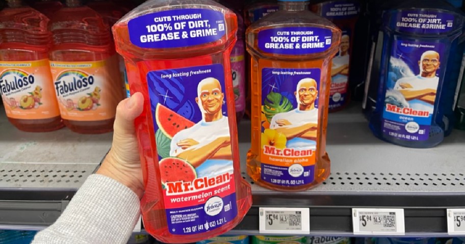 A hand holds a bottle of Mr. Clean floor cleaner with watermelon scent on a store shelf. Other scents are nearby.