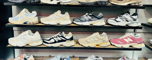 A display of 16 pairs of New Balance sneakers in various colors, arranged on four shelves. The shoes feature diverse designs.