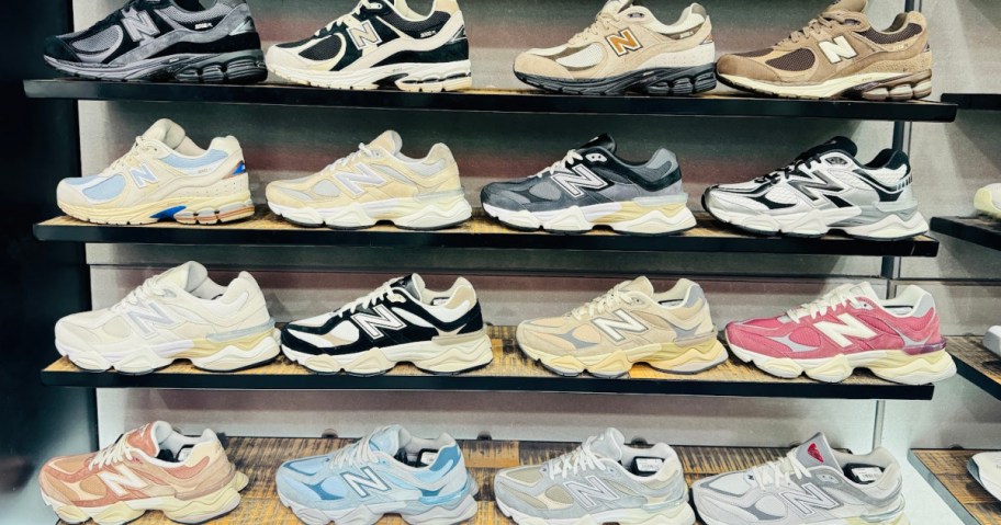 A display of 16 pairs of New Balance sneakers in various colors, arranged on four shelves. The shoes feature diverse designs.