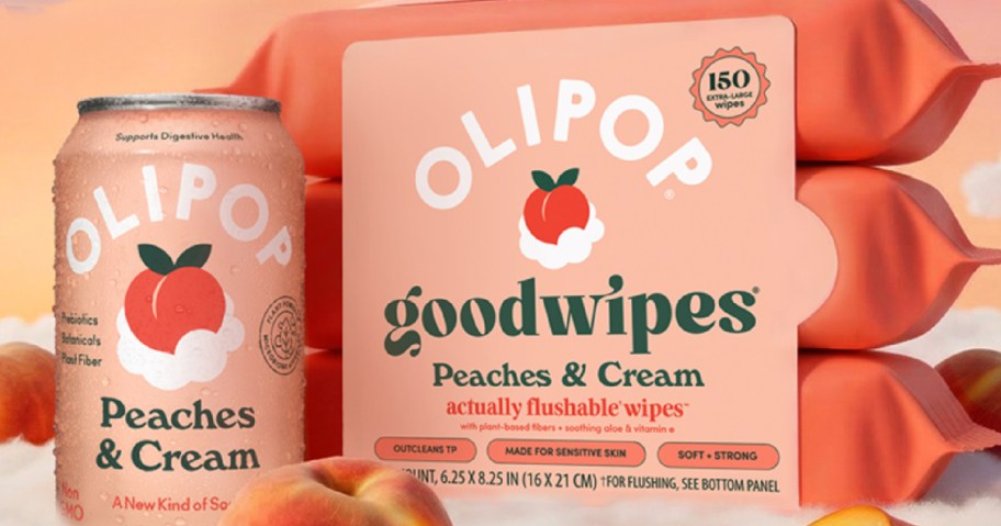 A can of Olipop Peaches & Cream soda next to a multi-pack of Olipop x goodwipes Peaches & Cream flushable wipes, displayed with fresh peaches against a soft, cloud-like background.