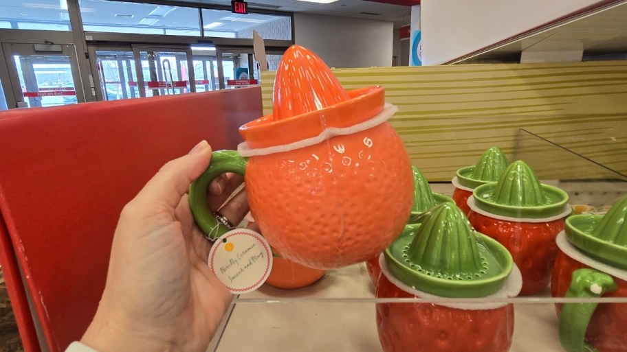 Woman's hand holding orange shaped ceramic cup with juicer lid