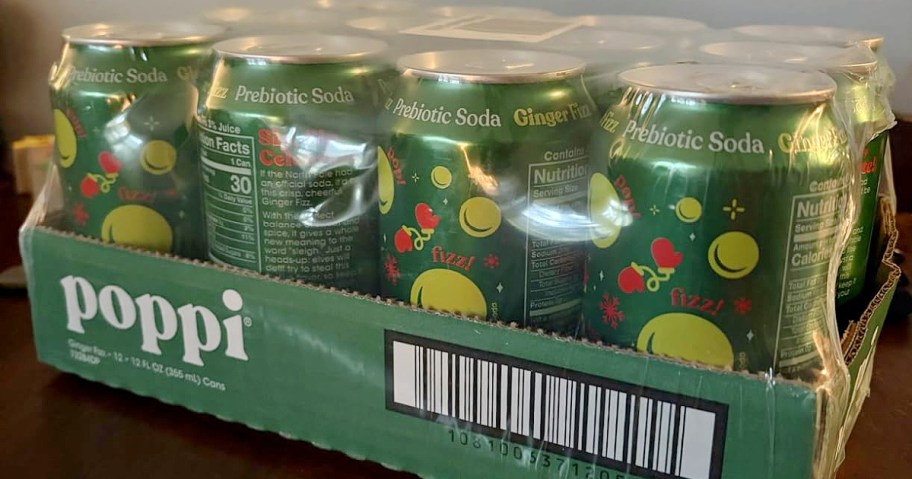 A 12-pack of green cans of poppi brand prebiotic ginger lime soda in transparent plastic wrap on a table.