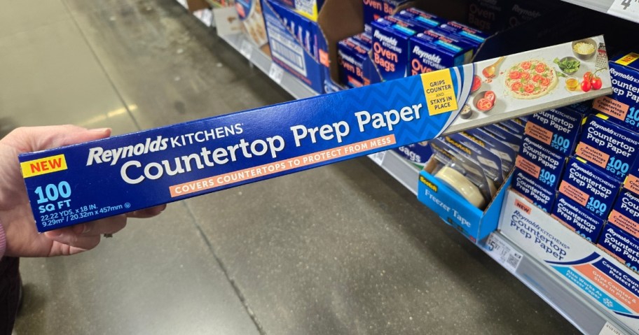 Hand holding a pack of Reynolds counter prep paper in store aisle