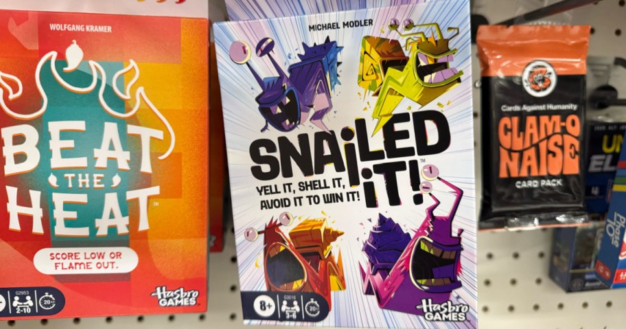Boxed games on a shelf include "Beat the Heat" and "Snailed It!" with vibrant, playful designs. A "Clam-O-Naise" card pack sits to the right.