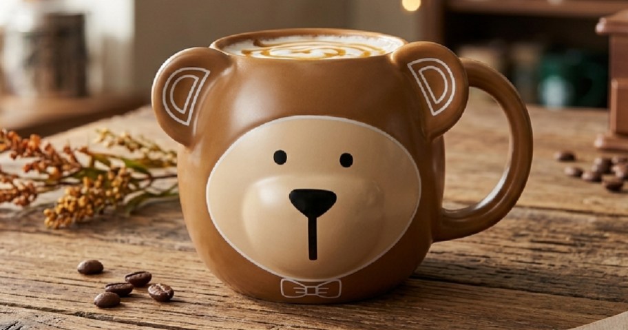 A brown bear-shaped mug with a cute design, placed on a wooden table with coffee beans and decorative plants in the background.
