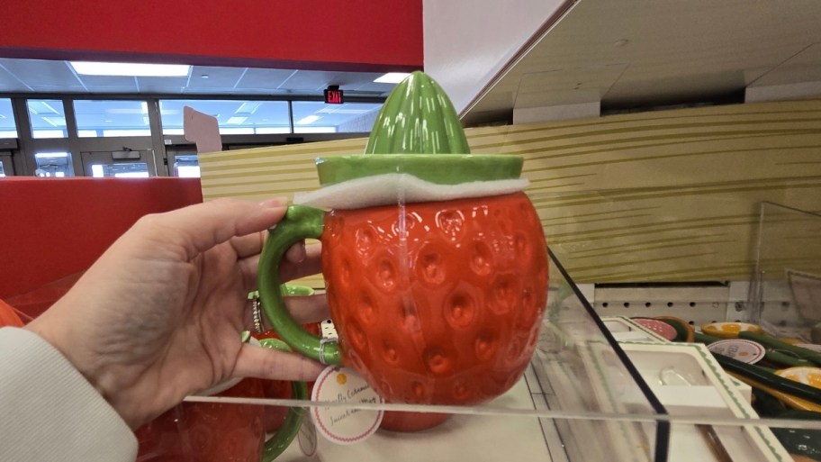 Woman's hand holding strawberry shaped ceramic cup with juicer lid