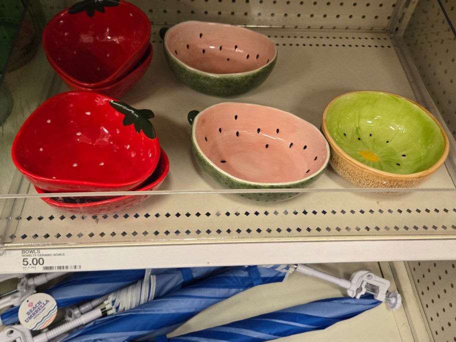 Ceramic bowls shaped like strawberries, watermelons, and kiwis are displayed on a store shelf. Vibrant and playful, $5 price tag is visible below.