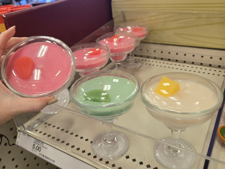 Candles shaped like margaritas in glass cups. They are pink, green, and white, with wax toppers resembling fruit. Priced at $5.00 each.