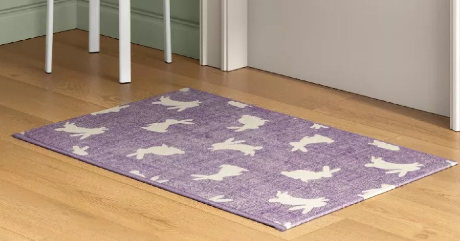 Purple rug with white bunny silhouettes on a light wooden floor next to white chair legs.