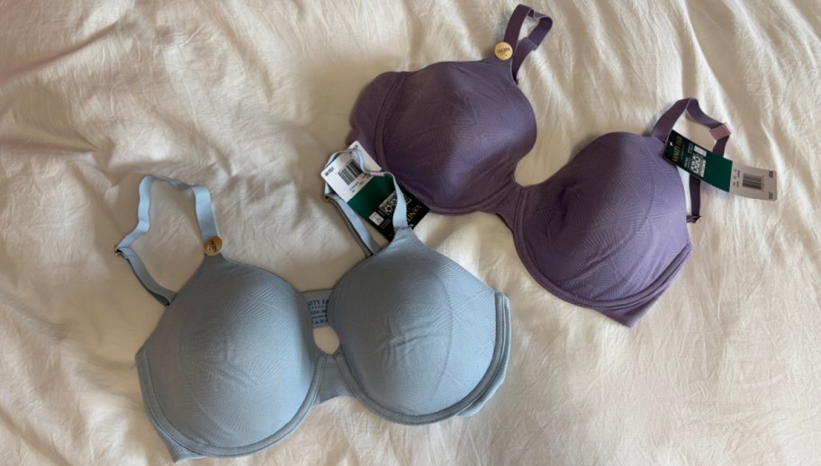 Two bras with tags are displayed on a white fabric surface. One is light blue, the other is purple.