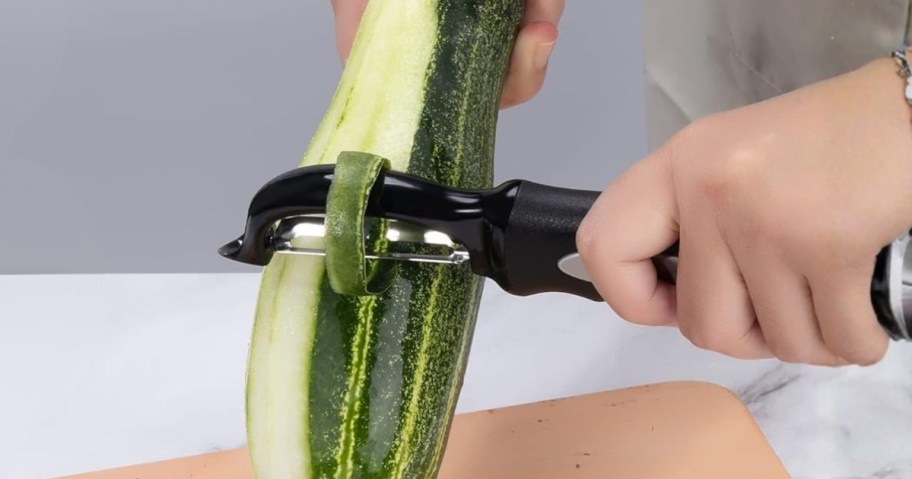 hand using a vegetable peeler to peel a cucumber