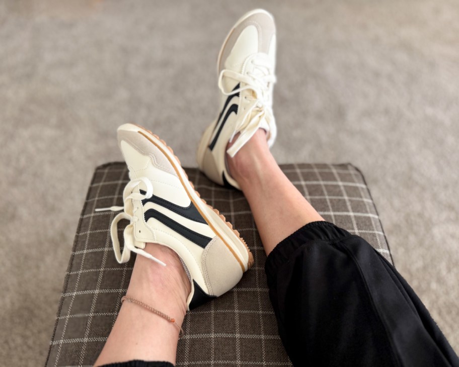 feet wearing black and white retro sneakers on brown ottoman