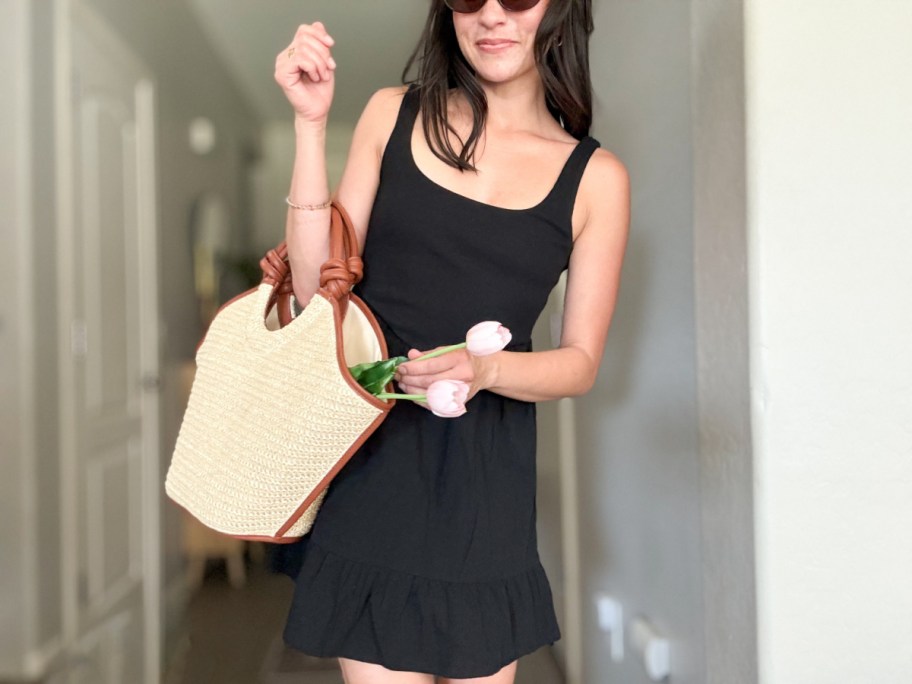 woman in black dress holding straw tote with flowers