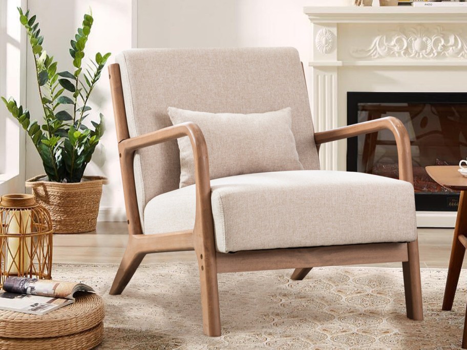A cozy living room scene features a beige armchair with wooden arms and legs, accented by a matching cushion. Nearby are a potted plant, fireplace, and soft rug.