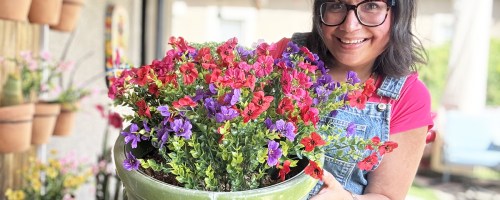 woman holding a planter with pink, red, and purple artificial flowers