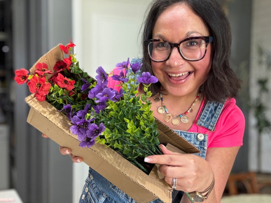 woman holding a box of red and purple artificial flowers