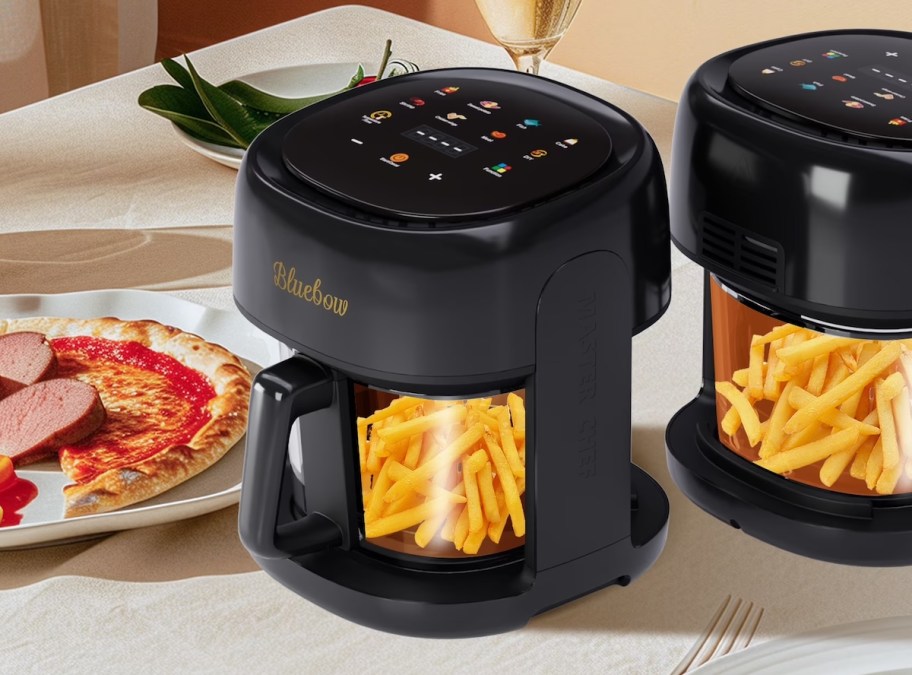 Two black glass air fryer sitting on countertop with french fries inside 